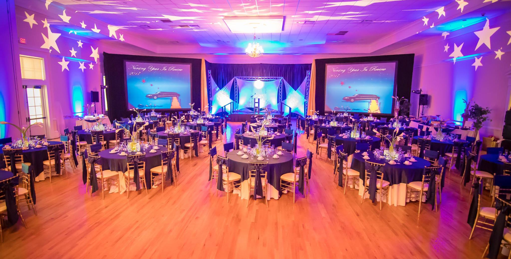 A ballroom set for a gala dinner, uplit in blue and violet