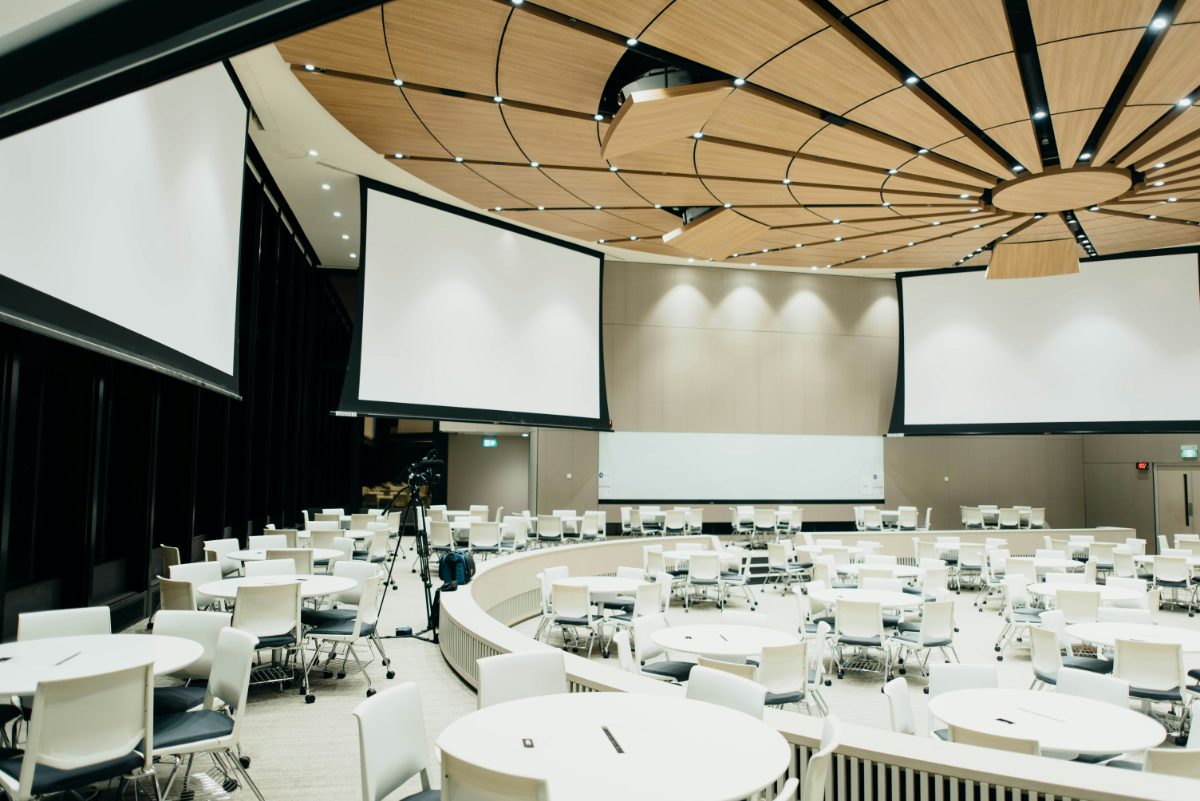 A tiered conference auditorium with projection screens and round tables